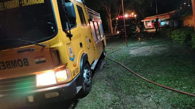 Camión de bomberos amarillo con logo en primer plano, personal en uniforme y luces encendidas en el ambiente de emergencia.