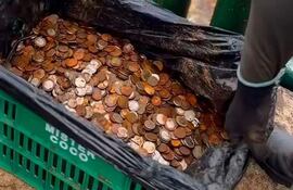 Manos sosteniendo un recipiente negro con monedas en un entorno urbano cercano a las Cataratas de Yguazú.