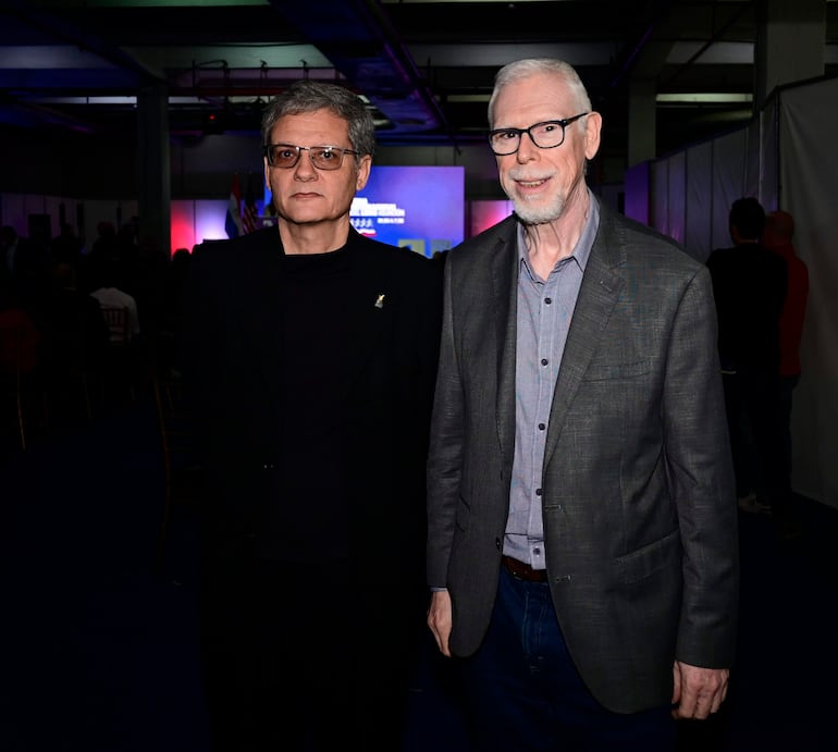 Alejandro Hernández con abrigo oscuro y gafas, sonriente en un evento formal con público a su alrededor.