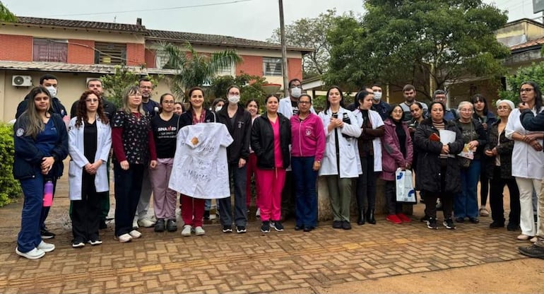 Grupo de médicos en exteriores, la mayoría con scrubs y batas blancas, sosteniendo un cartel con el mensaje 'Yo Mereço mis Mil Días'.