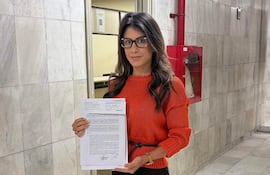 Mujer con suéter naranja y falda negra sosteniendo un documento frente a la Mesa de Entrada de la Corte Suprema.