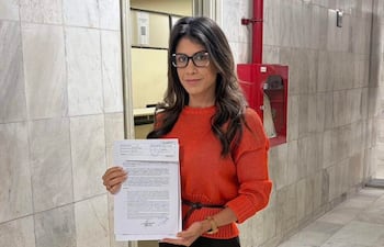 Mujer con suéter naranja y falda negra sosteniendo un documento frente a la Mesa de Entrada de la Corte Suprema.