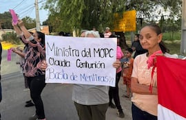 Mujer sostiene cartel con texto de reclamo mientras otros manifestantes levantan papeles coloridos en un ambiente urbano.