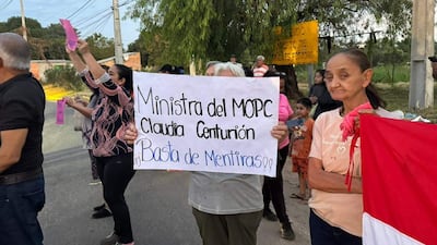 Mujer sostiene cartel con texto de reclamo mientras otros manifestantes levantan papeles coloridos en un ambiente urbano.
