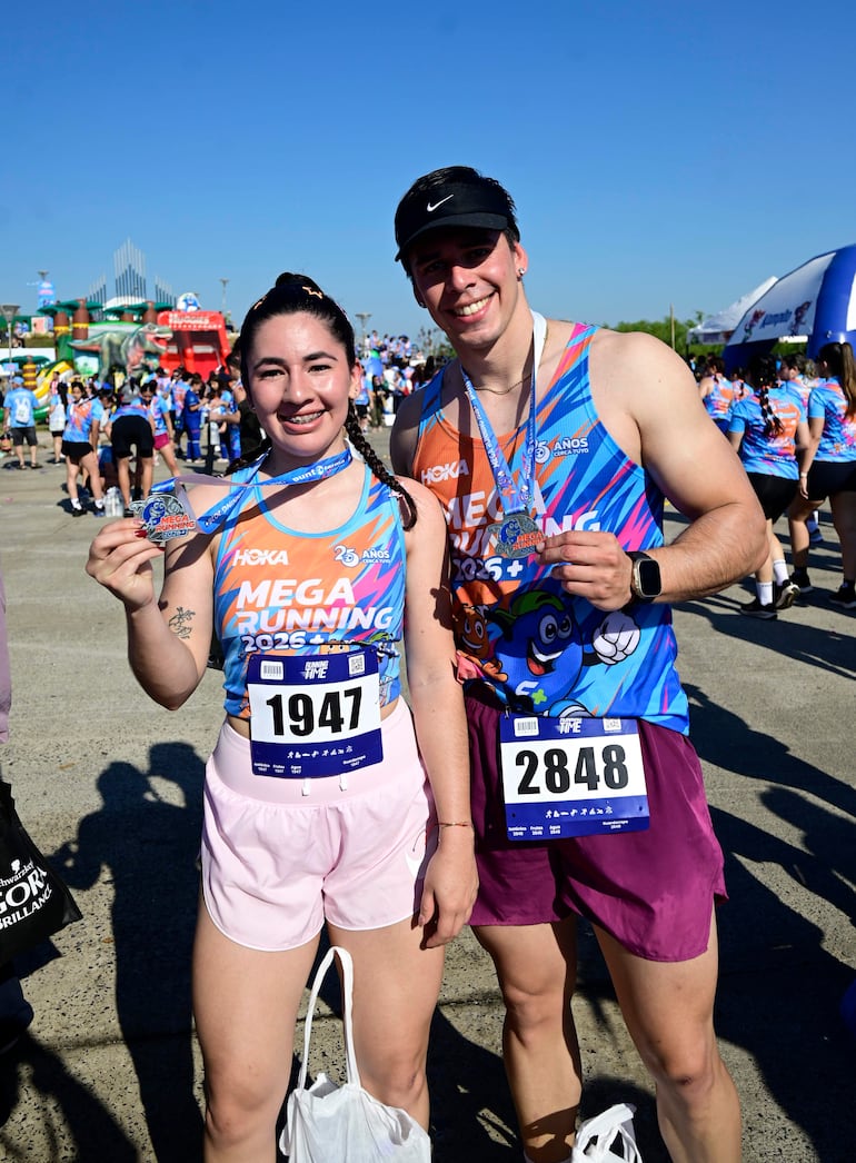 Mujer sonriente con medalla y camiseta azul y naranja junto a hombre feliz en evento deportivo al aire libre.