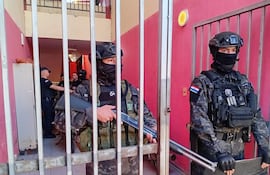 Dos agentes de seguridad armados, uniformados y en posición defensiva detrás de una reja, en un ambiente interior con paredes rojas.