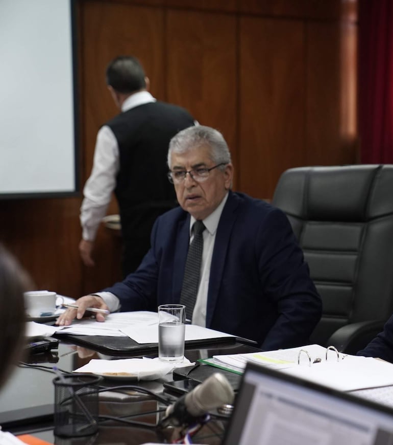 José Jara Rojas, hombre canoso en traje oscuro, discute con dos hombres en una sala de reuniones formales.