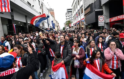 Mujer con trofeo y gente animada, todos con camisetas rojas y blancas y banderas de Paraguay en un ambiente festivo.
