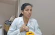 Mujer en uniforme blanco con manos juntas, mostrando interés en conversación, en oficina con objetos cotidianos en la mesa.