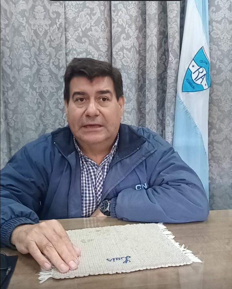 Luis Castillo, con chaqueta azul y camisa a cuadros, sentado en su despacho junto a una bandera.