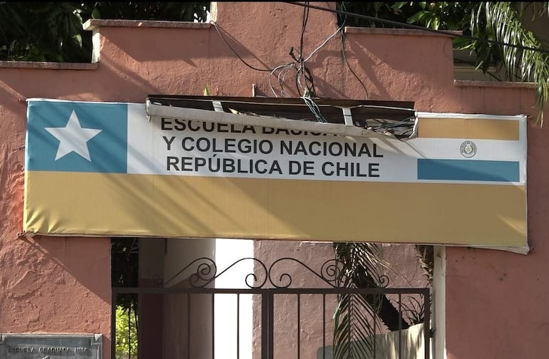 Cartel de la Escuela Básica y Colegio Nacional República de Chile con fondo en colores rojo, blanco y azul, frente a una pared rosa.
