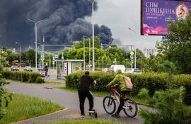 Varias personas permanecen en la calle mientras una densa columna de humo se eleva al fondo tras un presunto ataque con drones ucranianos, en Moscú.