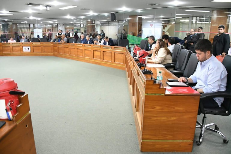 Juan Carlos Ozorio Admen frente a una mesa con carpeta roja, mientras Javier Pintos escucha atentamente en un ambiente formal.