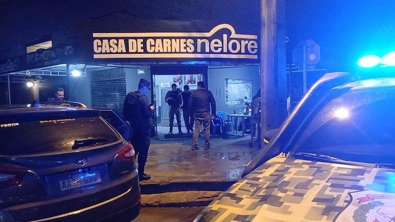 Hombres de atuendo oscuro conversan en la entrada de la carnicería 'Nelore', un policía en uniforme está presente.