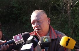 Pablino Giménez Galeano con cicatrices visibles en la cabeza, rodeado de micrófonos, en un entorno natural.
