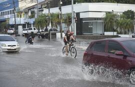 Un ciclista circula por Asunción en su bicicleta, sorteando vehículos a motor en un raudal.