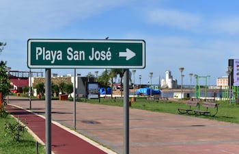 Cartel verde sobre césped, sin personas, con edificio blanco y estructuras de gimnasio al fondo.