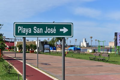 Cartel verde sobre césped, sin personas, con edificio blanco y estructuras de gimnasio al fondo.