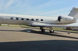 Avión privado blanco con detalles azules, estacionado en pista de aterrizaje bajo cielo azul.