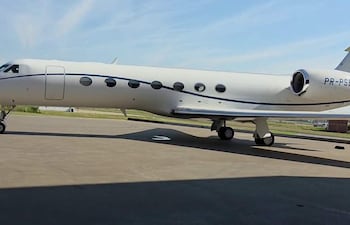 Avión privado blanco con detalles azules, estacionado en pista de aterrizaje bajo cielo azul.