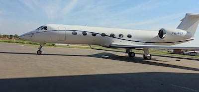 Avión privado blanco con detalles azules, estacionado en pista de aterrizaje bajo cielo azul.