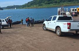 Grupo de seis personas en muelle, un hombre con casco supervisa actividades cerca de un vehículo Isuzu blanco.