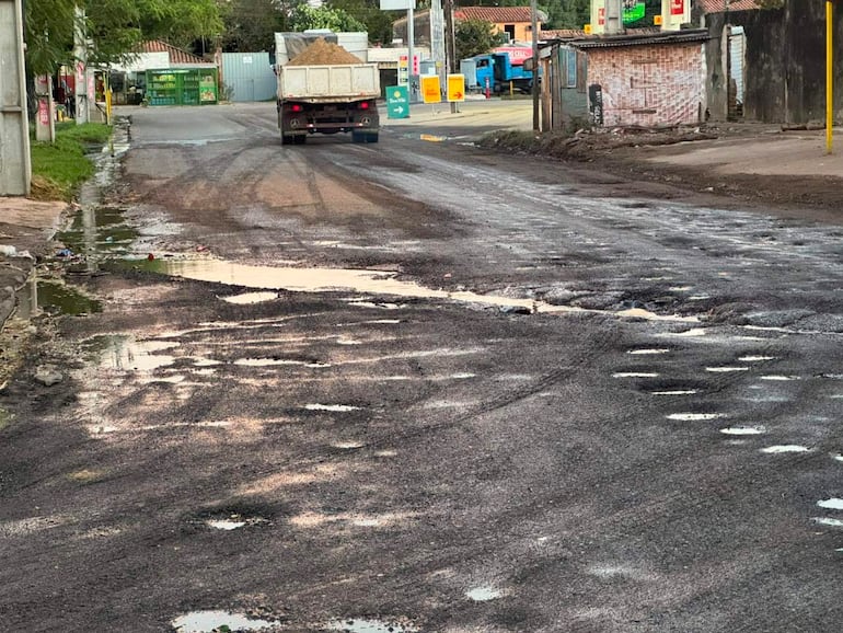 Calle con un camión circulando sobre baches y agua acumulada, ambiente urbano deteriorado.