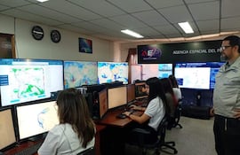 Cinco profesionales, cuatro mujeres y un hombre en chaqueta gris, trabajan concentrados frente a computadoras con gráficos en pantalla.