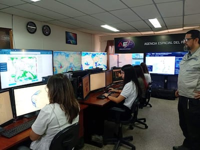 Cinco profesionales, cuatro mujeres y un hombre en chaqueta gris, trabajan concentrados frente a computadoras con gráficos en pantalla.