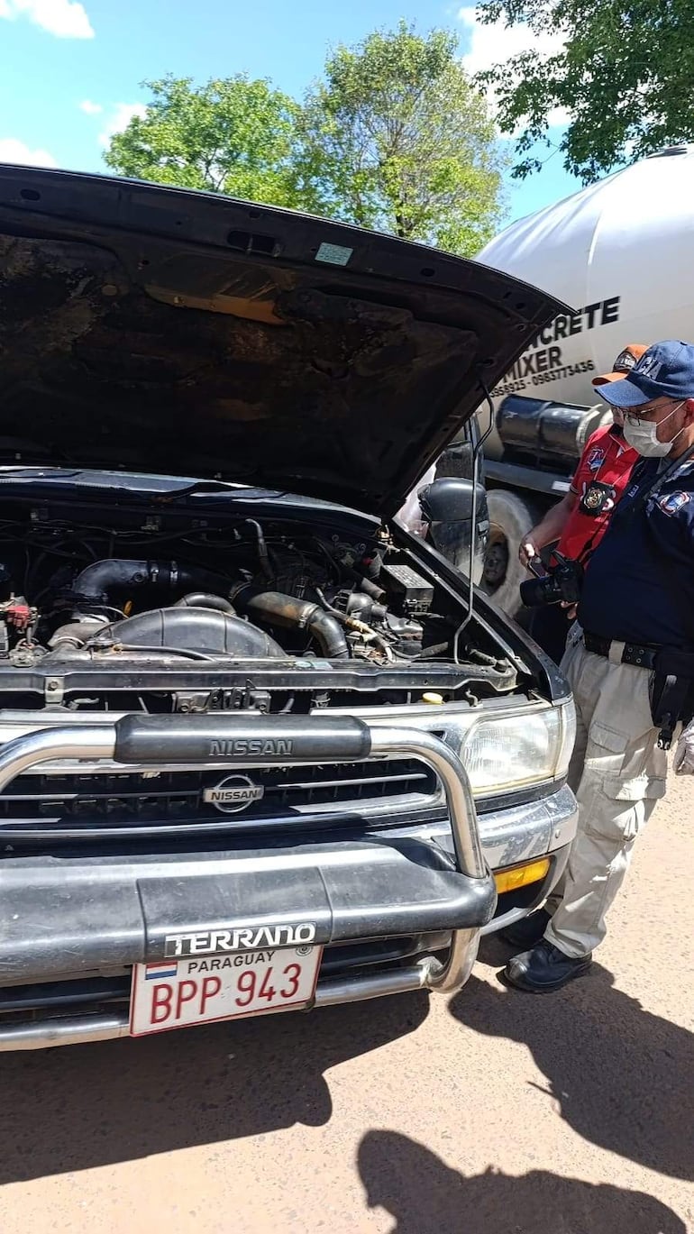 Tres personas inspeccionan el motor de una Nissan Terrano con capó abierto, un hombre observa y otro documenta el proceso.