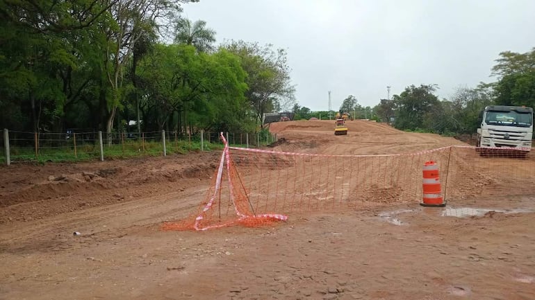 Máquina de construcción trabajando en terreno con rodillo y camión de transporte en un área de construcción rodeada de vegetación.