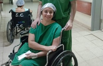 Patricia Sánchez en silla de ruedas sonríe mientras conversa con un hombre con ropa de hospital.