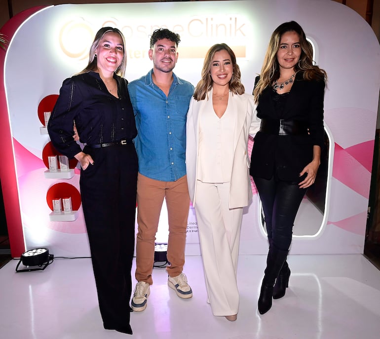 Cuatro personas sonrientes posan en un evento, vestidas elegantemente con atuendos variados frente a un fondo de la marca CosmeClinik.