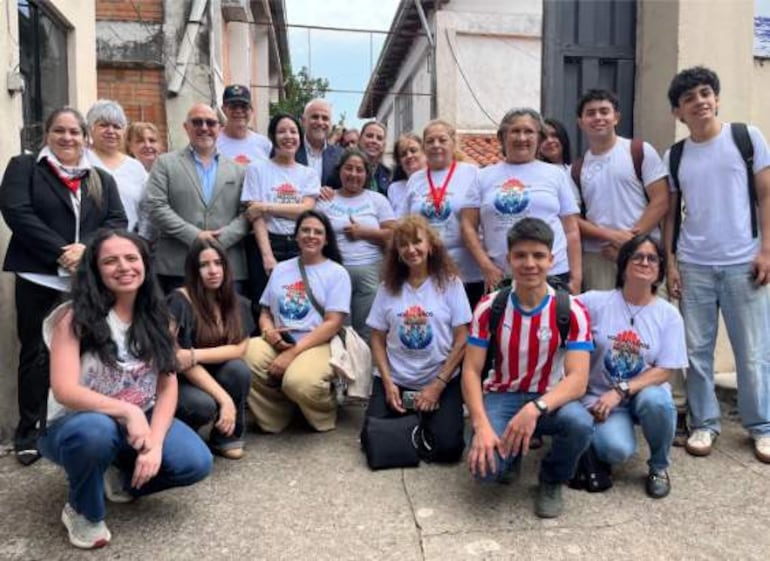 Grupo de aproximadamente 24 personas, muchas en camisetas blancas, posando en un ambiente exterior de un refugio temporal.