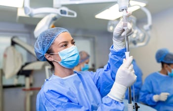 Una anestesióloga ajusta un dispositivo médico en un quirófano, acompañada de otros profesionales de la salud.