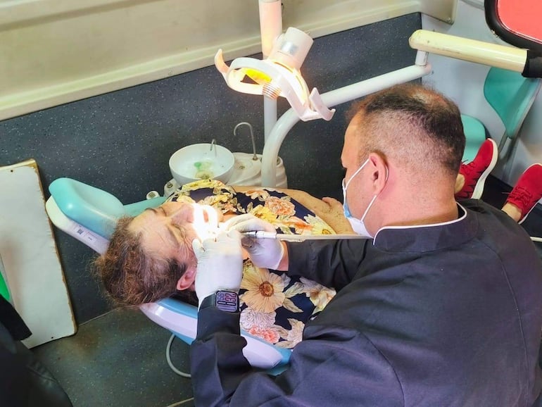 Mujer recostada en sillón dental con blusa floral, mientras un hombre con guantes y camisa oscura le realiza un procedimiento.