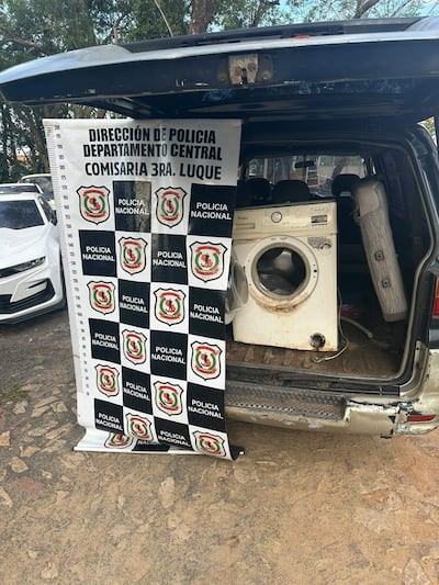 Interior de un vehículo policial con un lavarropas y un cilindro. Carteles de la Policía Nacional visibles.