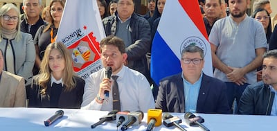 Acuña en camisa blanca y corbata gris habla al público, rodeado de asistentes en un evento oficial al aire libre.