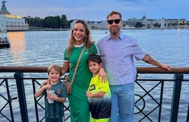 Antonella Volpe en vestido verde sonríe junto a dos niños y un hombre con camisa de cuadros en un muelle al atardecer.