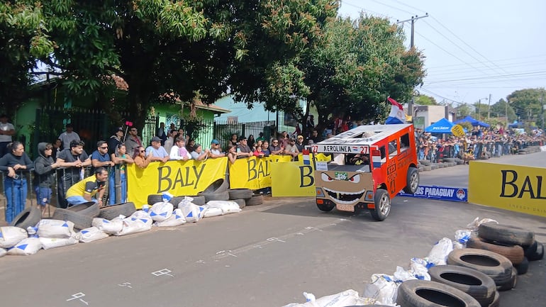 Auto de carreras número 27 con diseño caricaturesco, rodeado de una multitud que anima en el evento en Caaguazú.
