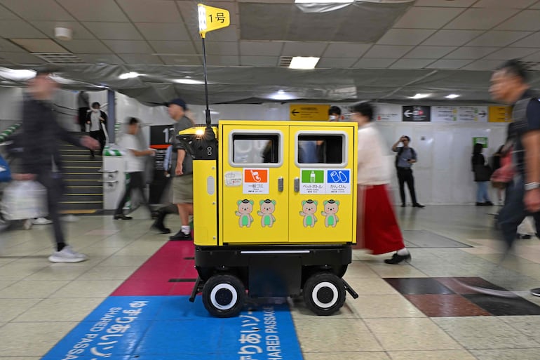 Personas caminan alrededor de un contenedor de basura robótico móvil que está siendo probado en el complejo de transporte de la estación de Shinjuku, en Tokio, el 18 de septiembre de 2026.