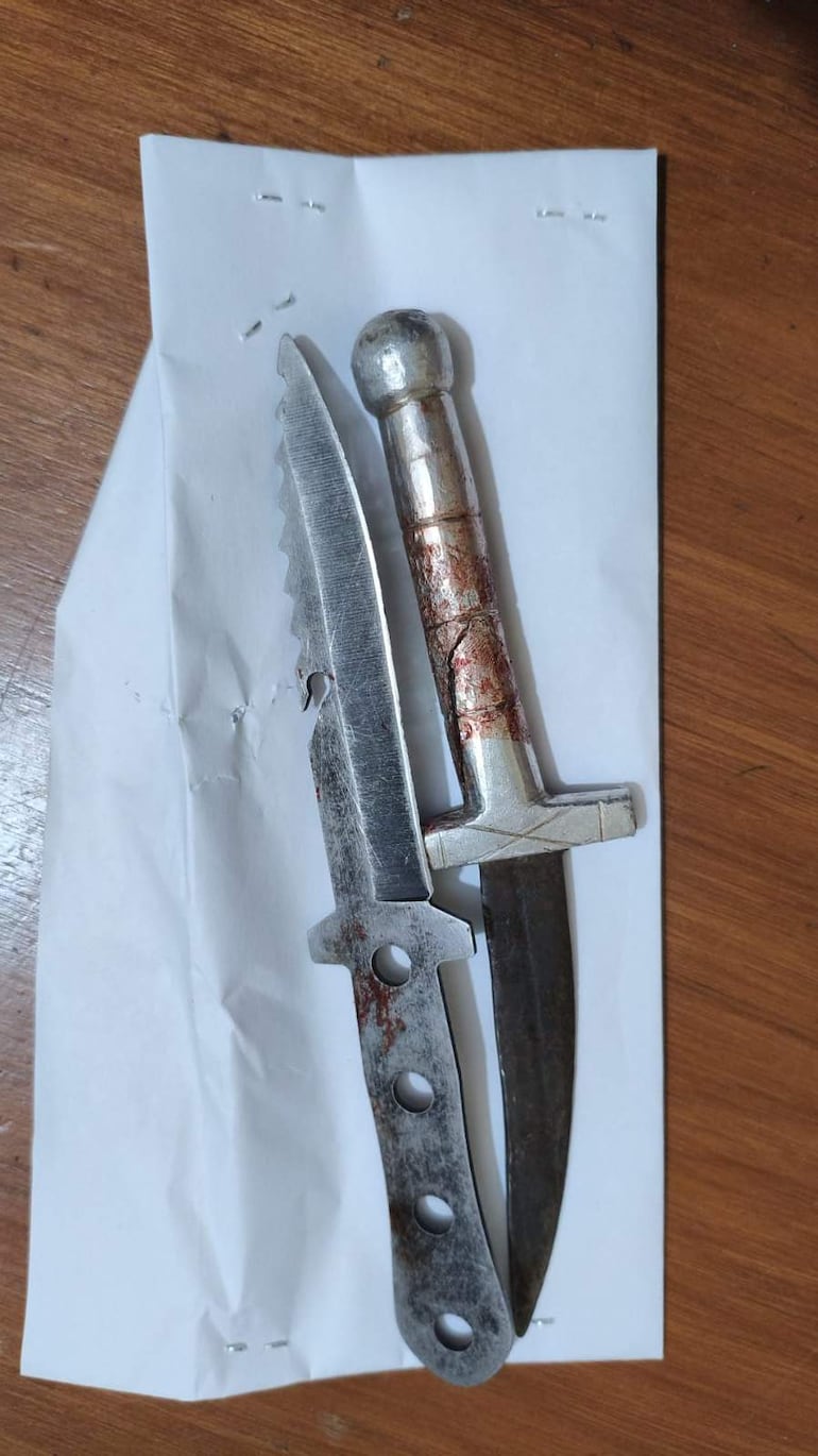 Dos cuchillos metálicos con manchas rojas en una superficie de madera, sobre una hoja de papel arrugada.