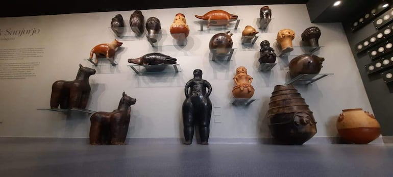 Exhibición de esculturas y cerámicas en un ambiente moderno con iluminación que resalta las obras en tonalidades terracota y negro.