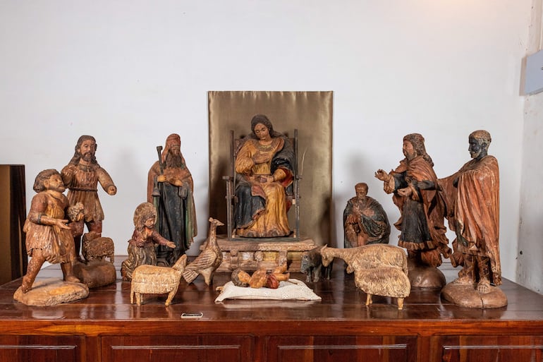 Figuras escultóricas de madera dispuestas en altar, destacando a una Virgen María en trono con vestimenta roja y dorada.