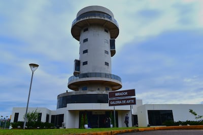 Edificio en forma de torre con señales que indican 'MIRADOR' y 'GALERIA DE ARTE'. El cielo está nublado.