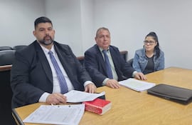 Nery Villalba con barba y traje oscuro, Ricardo Paredes en camisa clara y saco oscuro, Ada Arasy Ruiz Díaz con gafas en chaqueta de mezclilla, sentados en mesa con documentos.