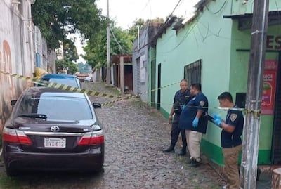 Agentes del Departamento de Criminalística inspeccionan el vehículo del oficial de la Policía Nacional.