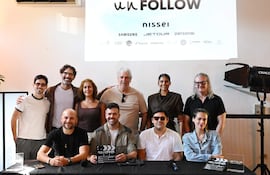 Once personas en un evento, algunos sentados sosteniendo un megáfono y un clapboard, luciendo felices en un ambiente decorado con logos.