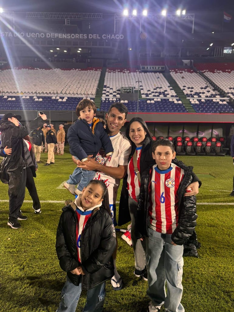 Cinco personas, entre ellas un hombre con un niño y una mujer, lucen camisetas rojas y blancas en un ambiente festivo.
