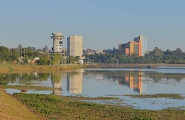 Paisaje urbano junto a un cuerpo de agua, con edificios altos y vegetación en los bordes, sin personas visibles.